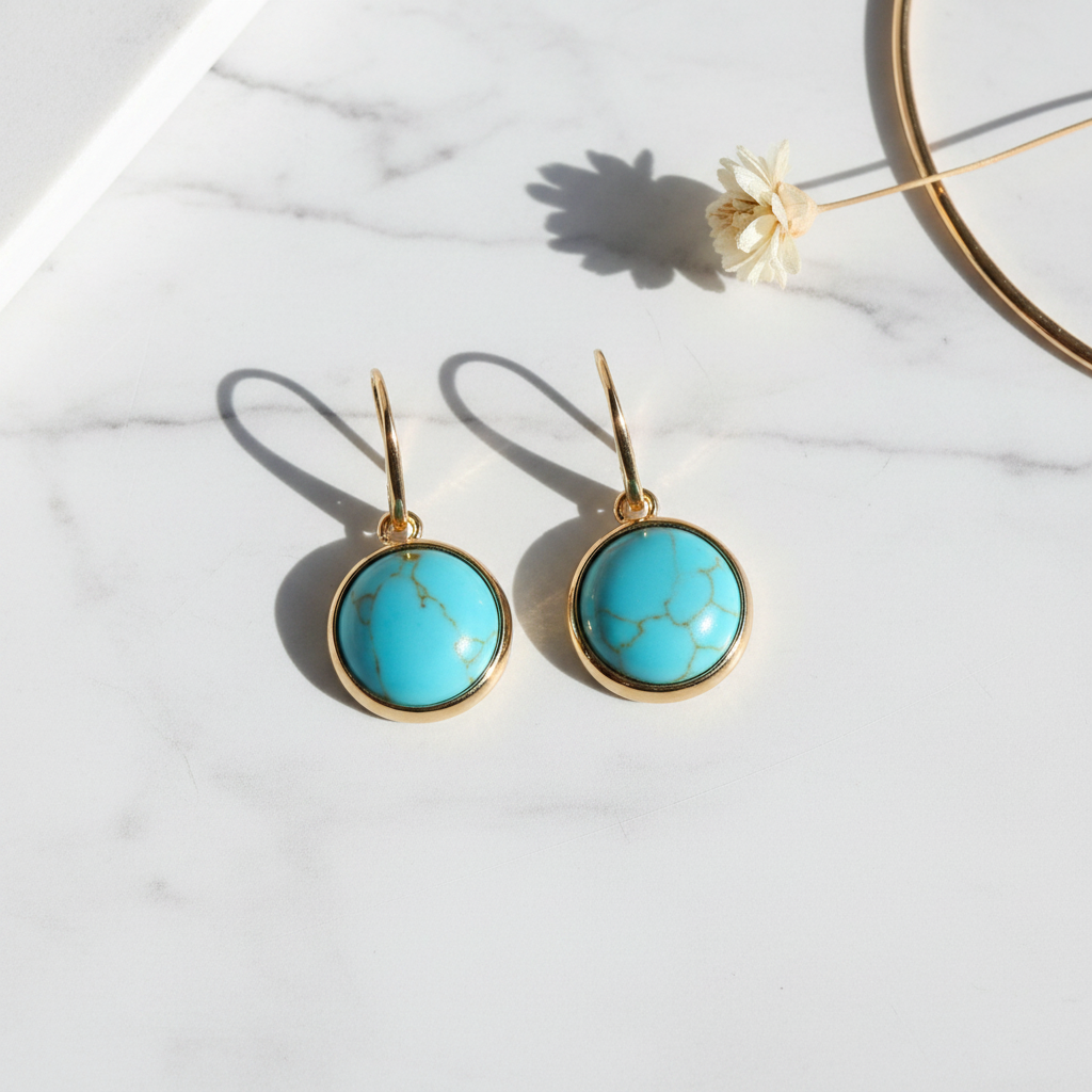 Oceania Sol Earrings - round turquoise cabochon in gold bezel setting with gold hook wires, flatlay on white marble